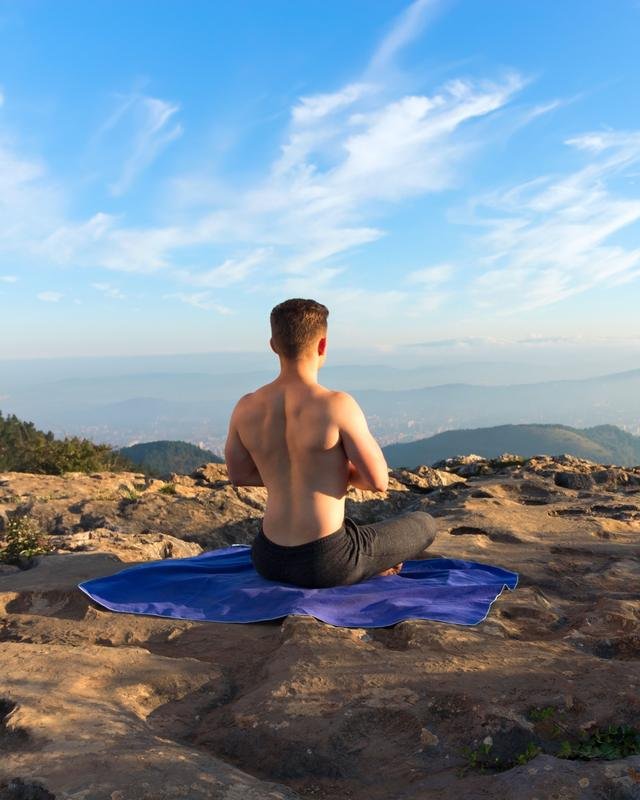 A man sitting cross-legged on a mountain top, breathing calmly