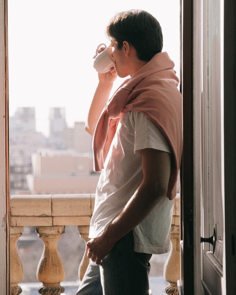 A man drinking his morning coffee at an open balcony door in soft sunlight