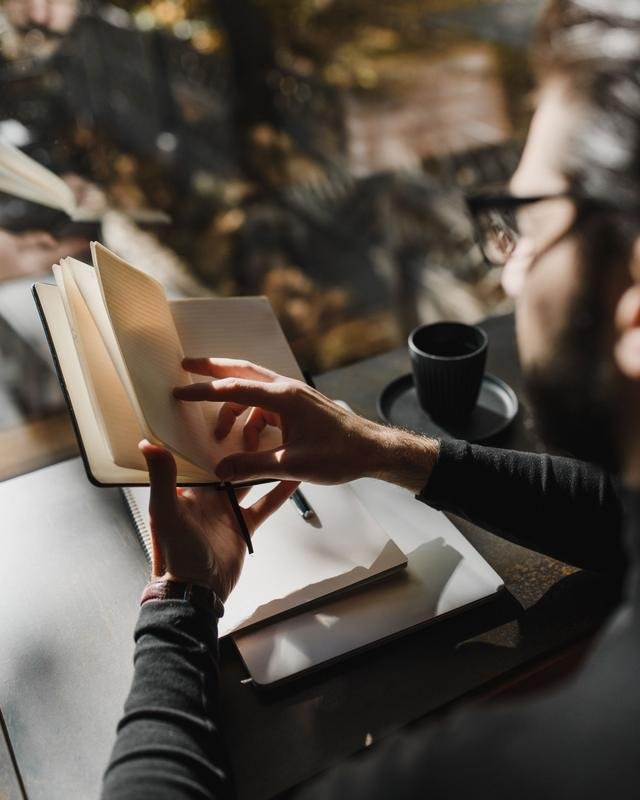 A man turning the pages of a notebook beside a cup of coffee