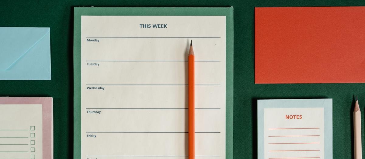A weekly planner page and pencil on a deep green desk