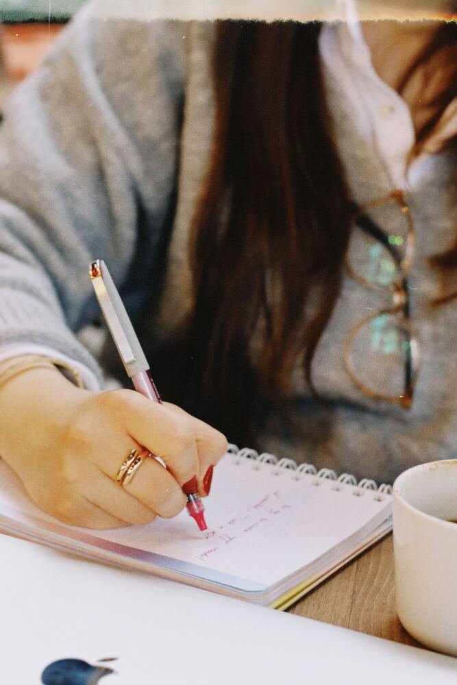 A hand writing in a journal beside a cup of coffee