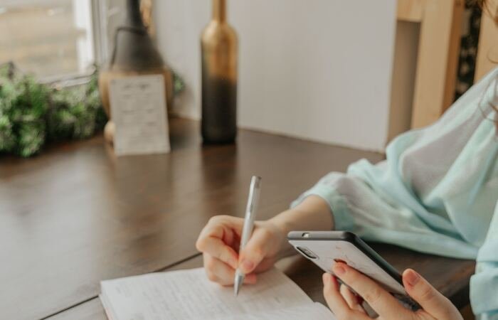 A hand writing in a journal beside a phone