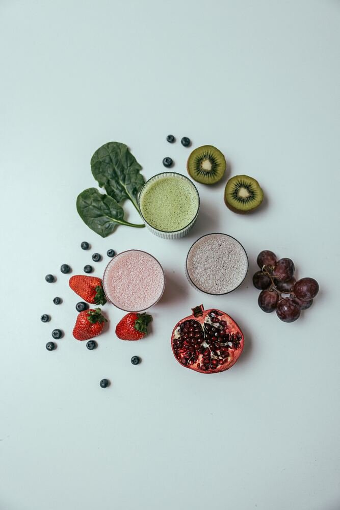 Smoothies and fresh fruit including berries, kiwi and pomegranate, laid flat