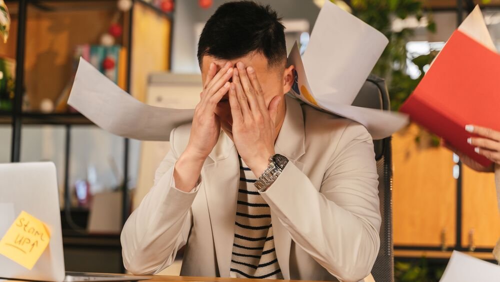 A tired man resting his head on his arms at an office desk